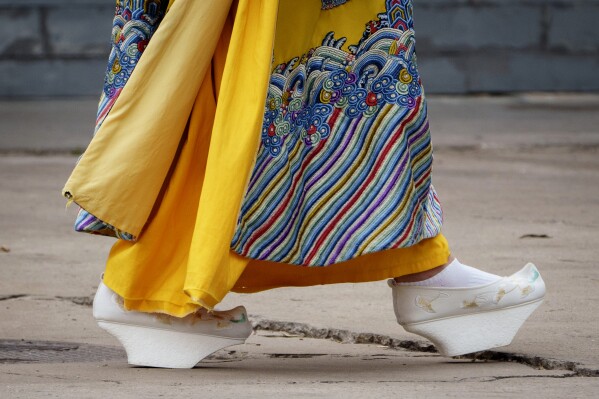 A Chinese woman walks dressed in Qing Dynasty attire with Manchu platform shoes near the Forbidden city in Beijing, China, Sunday, July 21, 2024. (AP Photo/Vincent Thian)