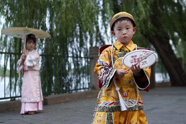 Chinese children dressed in Qing Dynasty royal attire stands for photographs at Beihai park in Beijing, China, Sunday, July 28, 2024. (AP Photo/Vincent Thian)