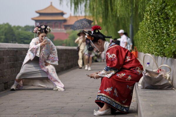 A Chinese girl dressed in Qing Dynasty attire takes photographs of another near the Forbidden city in Beijing, China, Sunday, July 21, 2024. (AP Photo/Vincent Thian)