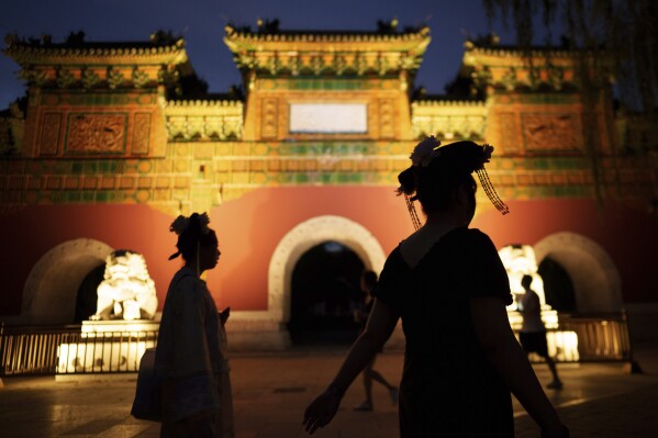 Chinese women dressed in Qing Dynasty attire walk in front of a traditional gate at Beihai park in Beijing, China, Sunday, July 28, 2024. (AP Photo/Vincent Thian)