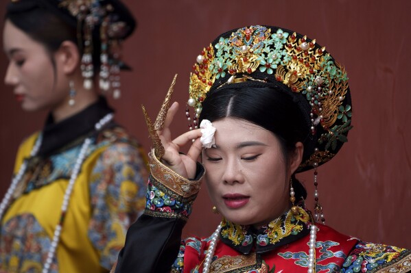 A Chinese woman dressed in Qing Dynasty attire wipes her sweat while posing for photographs near the Forbidden city in Beijing, China, Sunday, July 21, 2024. (AP Photo/Vincent Thian)