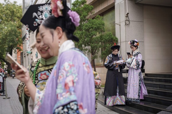 Chinese dressed in Qing Dynasty attire stand at a business building that provides one stop service for the traditional look in Beijing, China, Sunday, July 21, 2024. (AP Photo/Vincent Thian)