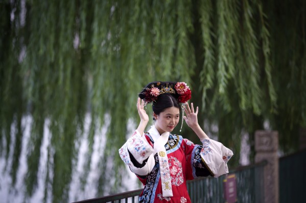 A Chinese woman dressed in Qing Dynasty attire and headdress stands for a photograph at Beihai park in Beijing, China, Sunday, July 28, 2024. (AP Photo/Vincent Thian)