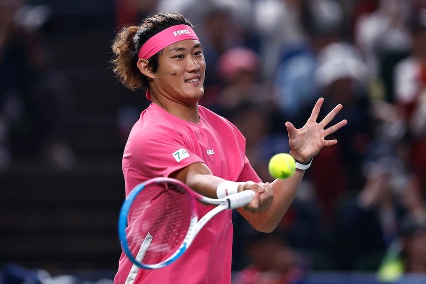 A Chinese tennis player wearing pink hitting a ball.