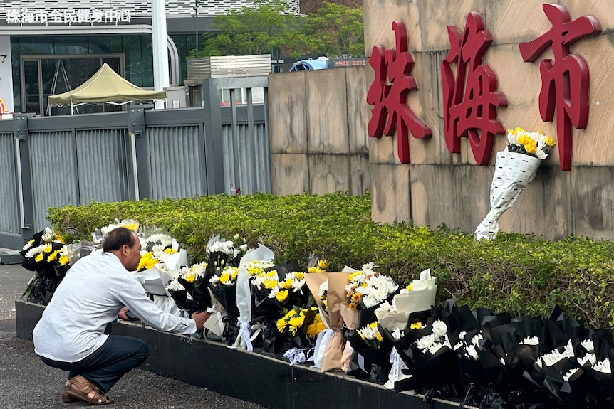 A man bends down while placing flowers among other bouquets