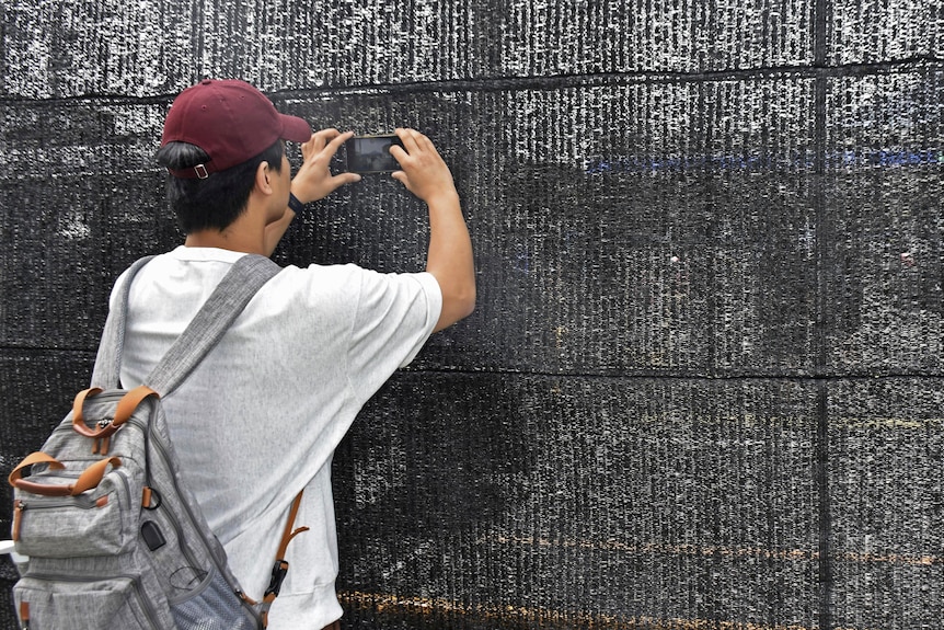 A person holds their phone up to a black screen to take a photo.