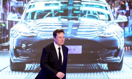 Elon Musk walks in front of a screen showing an image of a Tesla Model Y.