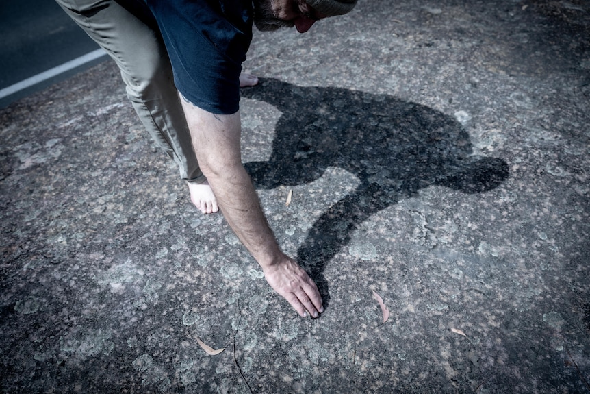 Shane Smithers stands barefoot on a large flat rock surface with engravings.