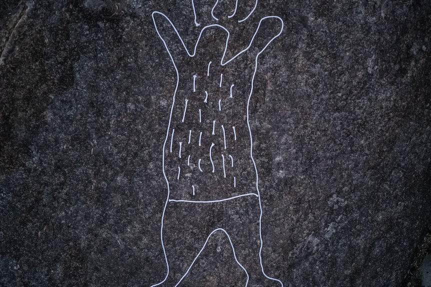 Light illuminates a figure outlined in white on a rock face.