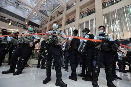 Police officers wearing masks stand in a shopping centre holding an orange cordon