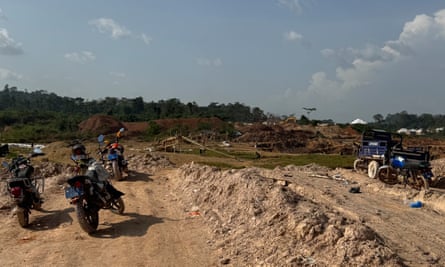 Motorbikes parked next to a dirt track of piled up sand near a mining site