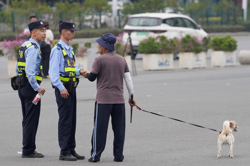 Two Chinese police officers talk with a man walking his dog