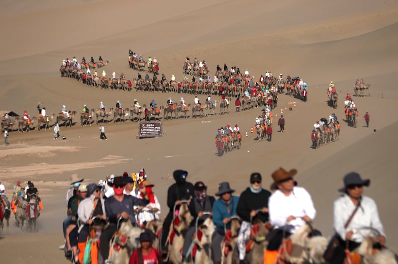 Tourists ride camels at the Mingsha Mountain and Yueya Spring area. Photograph: Zhang Xiaoliang/VCG via Getty 