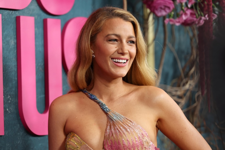 A blonde woman in a multi-coloured gown smiles 