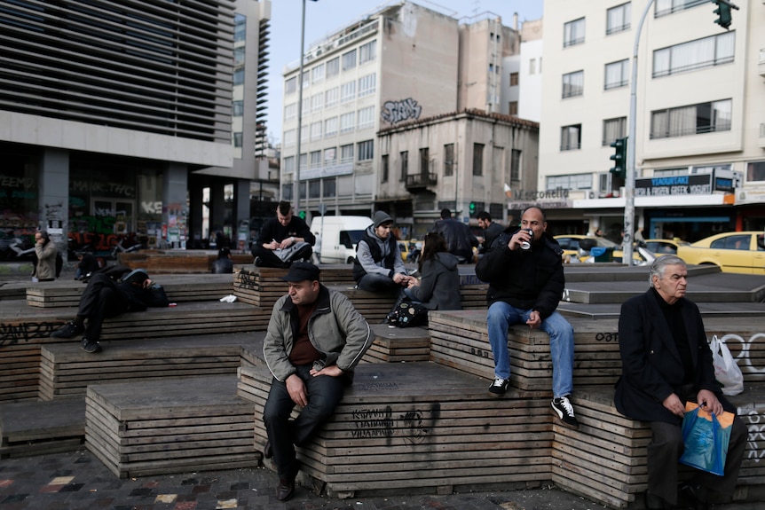 People sit on seats resting at a central square in Athens