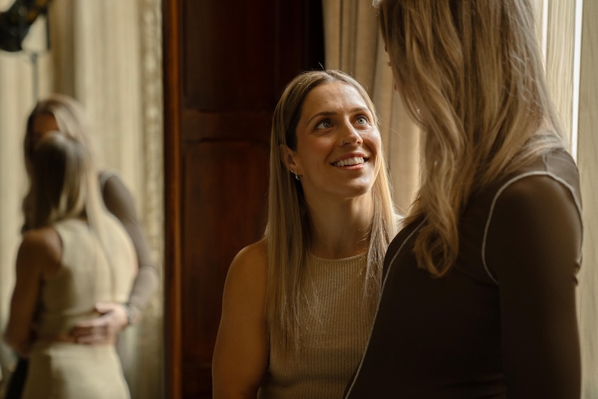 A blonde woman looks up smiling at another blonde woman