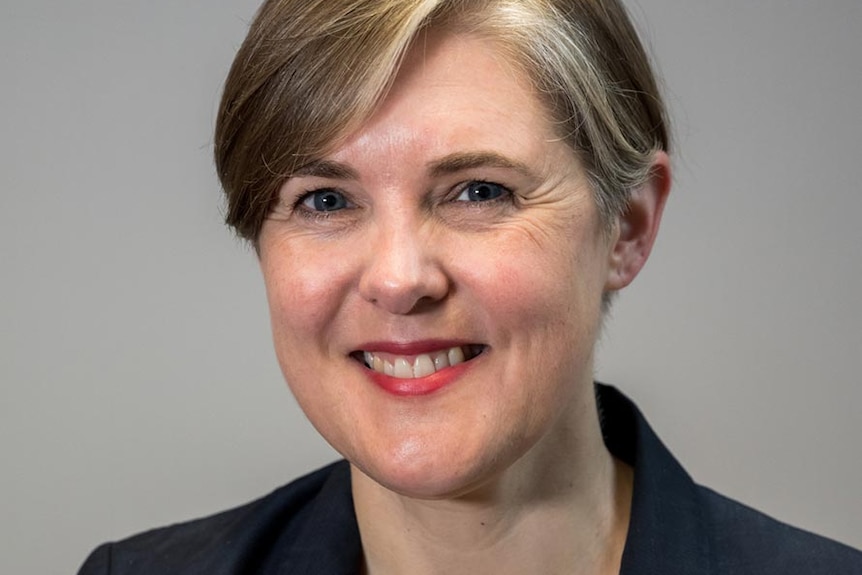 Headshot of woman Alison Reeves from the Grattan Institute, wearing a black blazer jacket. Standing against a grey background. 