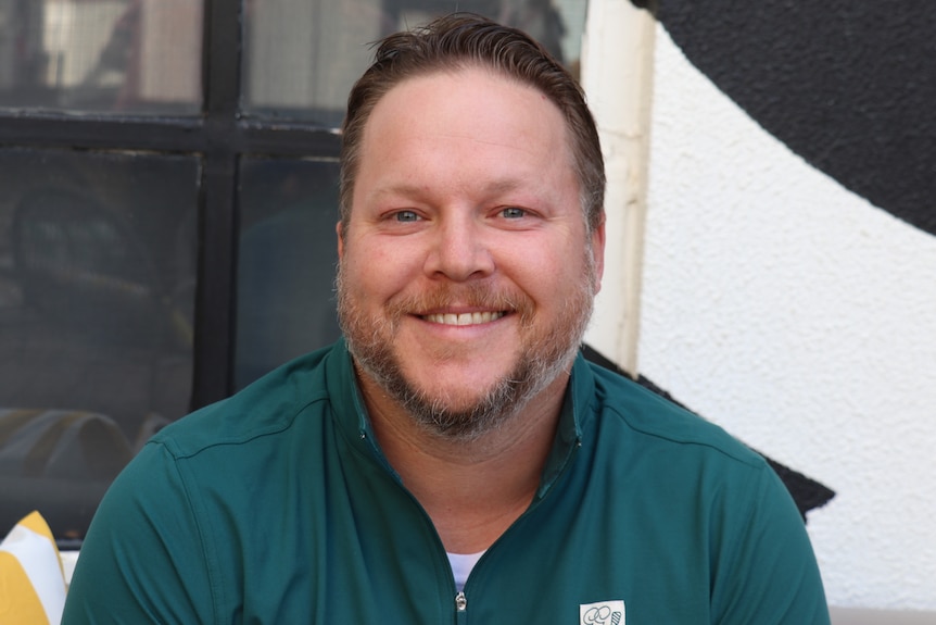 A man with a short greying beard smiles towards the camera. 