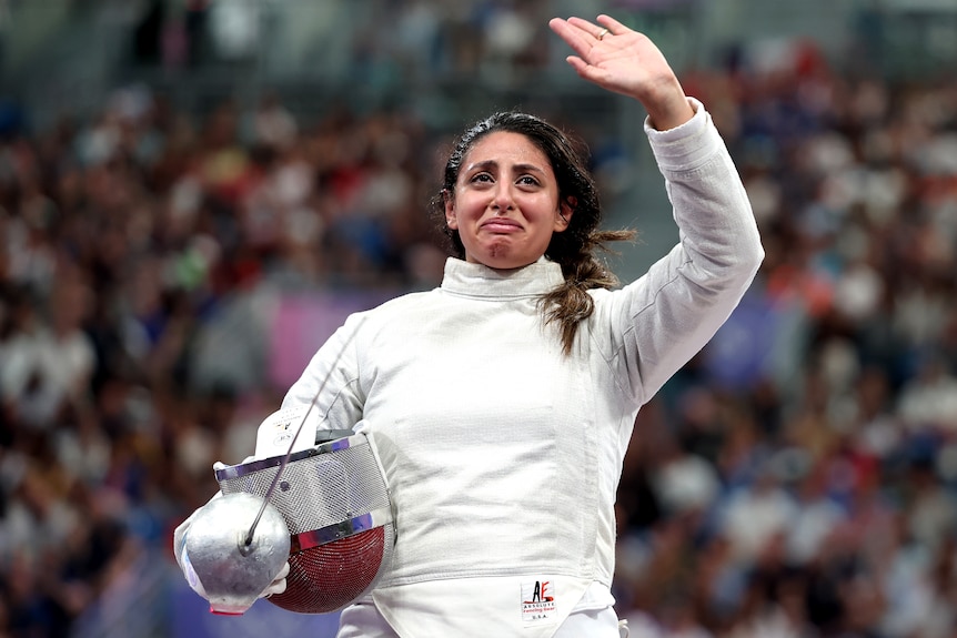 A woman waves to the fans having being eliminated from a fencing competition