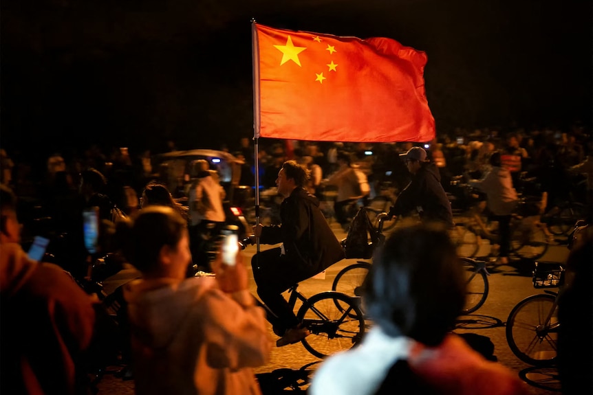 A man with a China red flag cycling at night.