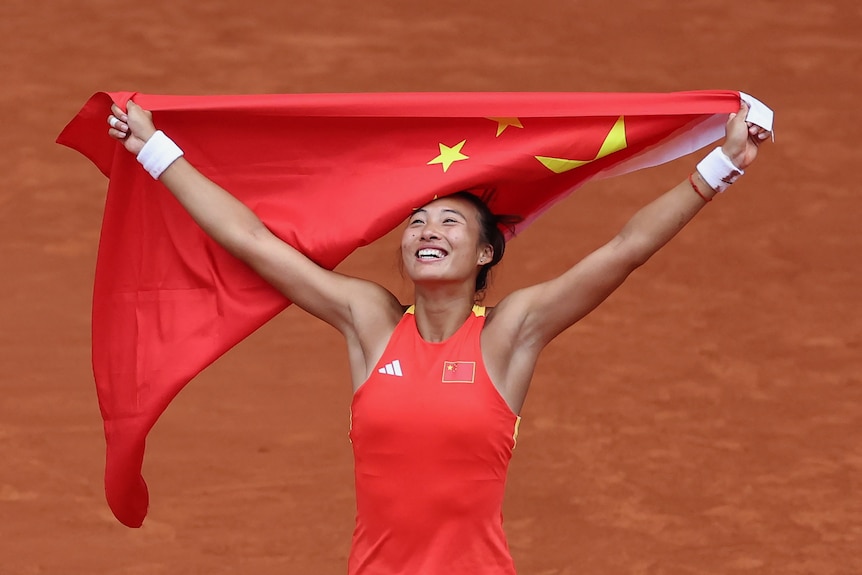 A woman in red dress holding Chinese flag above he head and smiling.